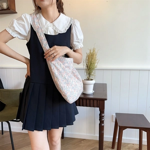 Close-up of small floral canvas crossbody bag styled with a white blouse and blue dress