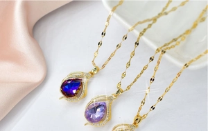 Close-up of three gold teardrop necklaces with blue and purple crystals on pink silk