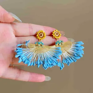 Détail de boucles d'oreilles tournesol avec breloque éventail dorée et pompons bleus