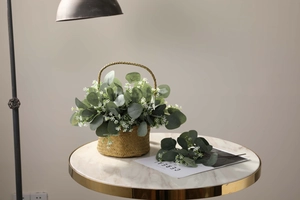Artificial eucalyptus leaves in a woven grass basket on a marble table with a Nordic style