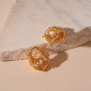 Macro detail of gold plated U-shaped hoop earrings with woven texture on stone display
