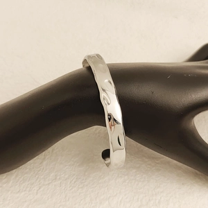 Minimalist silver hammered stainless steel open bangle displayed on a black mannequin hand