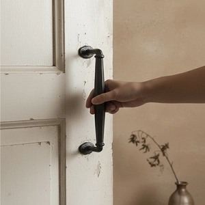 Vintage black cast iron door handle with matte finish on a rustic white wooden door