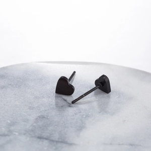 Minimalist matte black heart stud earrings set on a textured marble background display
