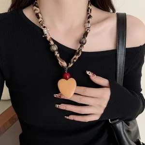 Close-up of leopard print fabric necklace with red bead and large wooden heart pendant
