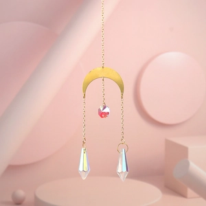 Detail of golden moon suncatcher with iridescent crystal prisms on pink geometric background