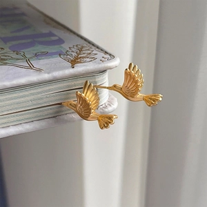 Artistic close-up of golden hummingbird studs tucked into vintage book pages