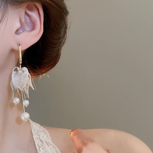 Close-up of floral acrylic earrings with dangling white pearls worn by a model