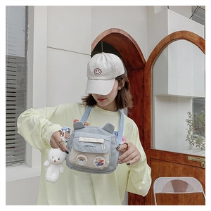 Detail of canvas crossbody bag with cartoon bear patch and plush pendant decoration
