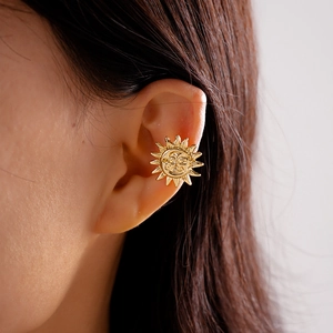 Macro view of gold sun face clip-on earring worn on ear without piercing needed