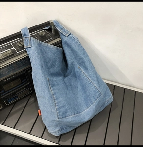 Detail of light blue washed denim tote bag with wide strap and orange side label