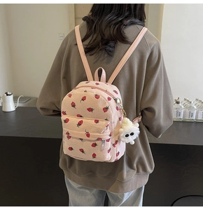 Detailed texture of pink corduroy backpack with cute strawberry patterns and plush charm