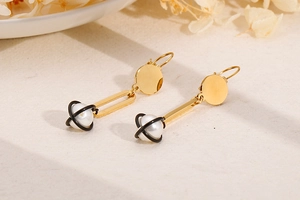 Detail of asymmetrical long gold pearl earrings with unique black planet cage design