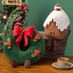Detail of plush Christmas wreath and gingerbread house doll pillows on a cozy wooden table