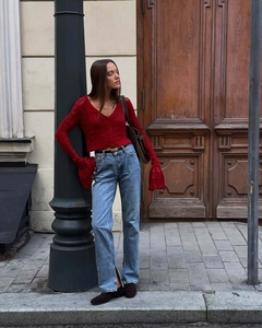 Detail of red V-neck cropped knit cardigan with ribbed texture and split leg denim jeans