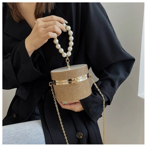 Close-up of golden rhinestone cylinder bag with large pearl handle and metal chain