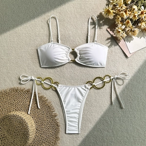 Vue à plat d'un bikini blanc avec anneaux dorés sur un fond d'été texturé beige clair