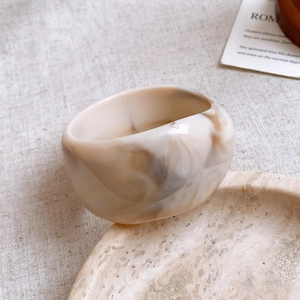 Macro view of wide resin bangle with cream and coffee marble texture on marble tray