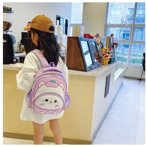 Rear view of lavender purple cartoon cat backpack worn by a child in a cozy cafe setting