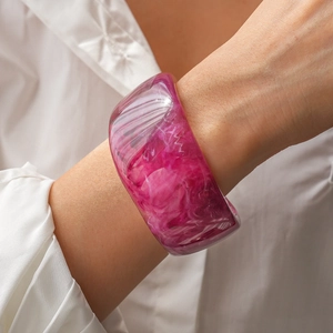 Macro shot of wide pink resin bangle with marble ink effect worn on model wrist