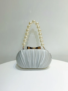 Nahaufnahme von Perlengriff und Goldschleife an silberner Plissee-Abendtasche