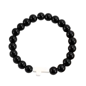 Macro detail of black beaded bracelet with a white cross pendant on a white background