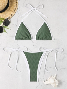 Flat lay of forest green textured triangle bikini set with white trim on stone surface