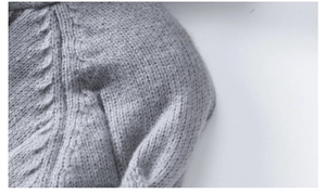 Detailed close-up of light gray cable knit sweater shoulder seams and thick wool texture