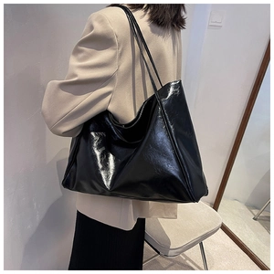 Close-up of large black tote bag in glossy faux leather showing soft texture and straps