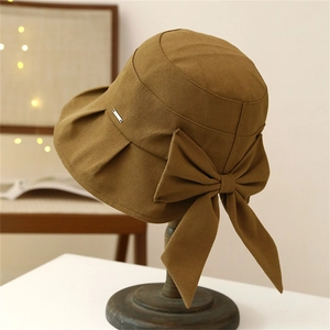 Caramel sun hat with large bow and metal logo on a vintage wooden stand