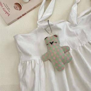 Detail of pink and green checkered plush bear charm hanging on a white canvas tote bag