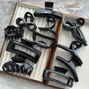 Collection of black plastic hair claws in various shapes displayed in a beige jewelry box