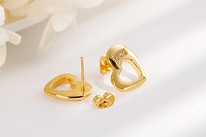 Detailed view of gold hollow heart studs with three small diamonds and butterfly backs