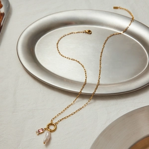 Detailed shot of golden pearl necklace with pink gemstone and baroque pearl on tray