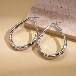 Detail shot of silver twisted teardrop hoop earrings on natural travertine marble background