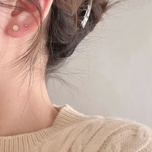 Close-up of minimalist gold-plated smiley face and round ball stud earrings worn by a model