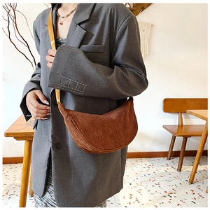 Brown corduroy crescent crossbody bag shown on a model in a cozy cafe setting