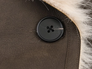 Close-up of black button on brown leather coat with cream faux fur lining details