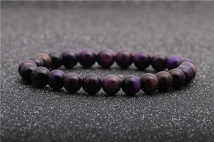 Dettaglio ravvicinato del bracciale con perline di occhio di tigre viola su sfondo nero