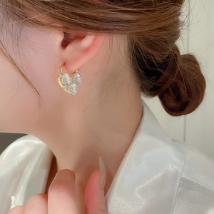 Elegant model shot of heart-shaped gold earrings with zircon and flower details