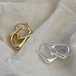Detailed close-up of gold and silver S925 sterling silver U-shaped earrings on beige fabric