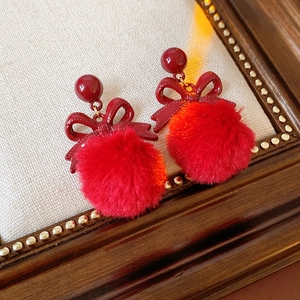 Detailed view of red pom-pom earrings with a metallic bow on a textured background