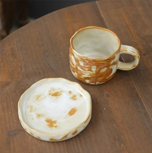 Macro detail of handmade stoneware coffee cup with orange swirl glaze on wooden table