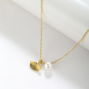Macro shot of gold ginkgo leaf pendant and elegant white pearl on a fine chain