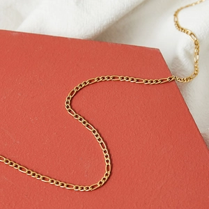 Golden titanium steel Figaro chain necklace displayed on a textured background