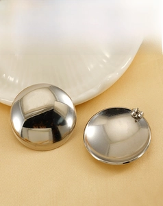 Gros plan de boucles d'oreilles rondes argentées sur une surface en satin jaune