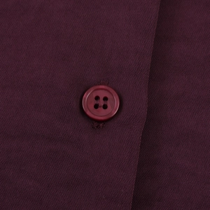 Macro shot of a matching four-hole button stitched on dark red satin fabric texture