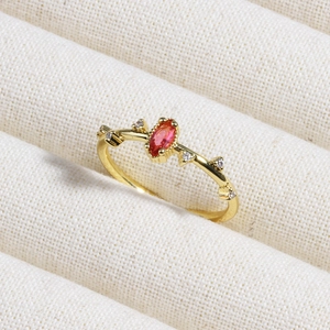 Macro shot of an oval red gemstone ring with small diamonds on a white fabric background