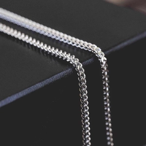 Close-up of polished silver stainless steel wheat chain necklace on a black box