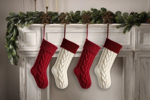 Detail of four cable knit Christmas stockings hanging on a white fireplace with decor